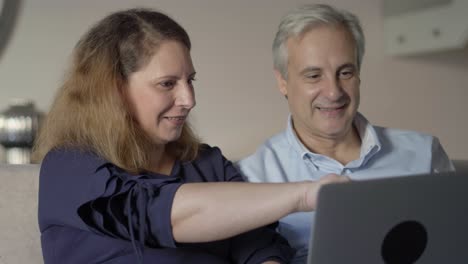 Positive-mid-adult-couple-with-laptop-discussing-new-online-app